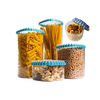 In fünf durchsichtigen Behältern mit blauen Deckeln befinden sich Spaghetti, Nudelröhrchen, Kichererbsen, Nussmischungen und Walnüsse. Die Behälter sind vor einem weißen Hintergrund angeordnet.