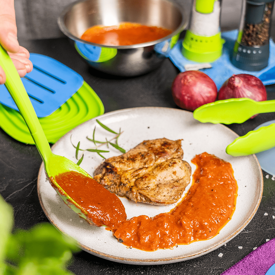 Grilled chicken breast on a plate with tomato sauce being spooned beside it, kitchen items in background.