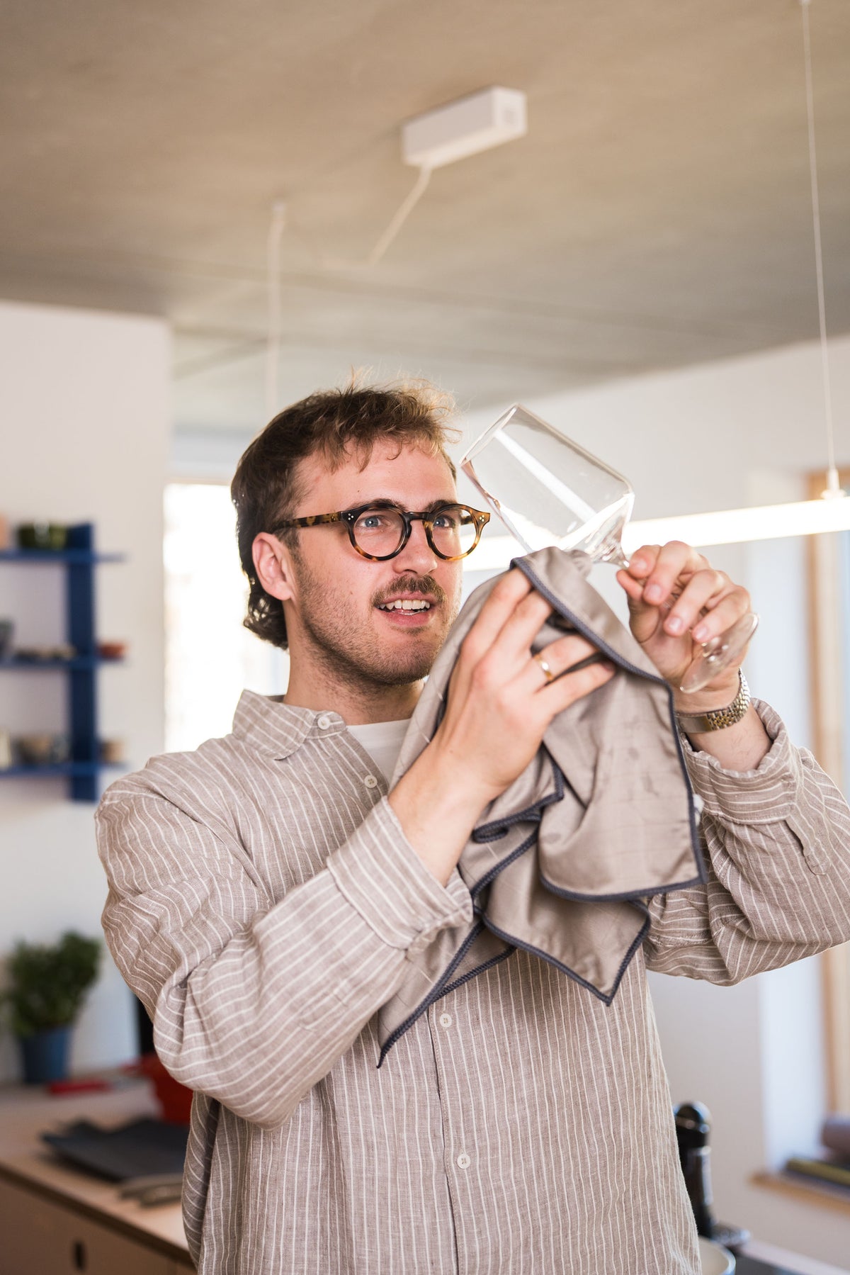 Eine Person mit Brille trocknet in einer Küche ein Weinglas mit einem Tuch ab.