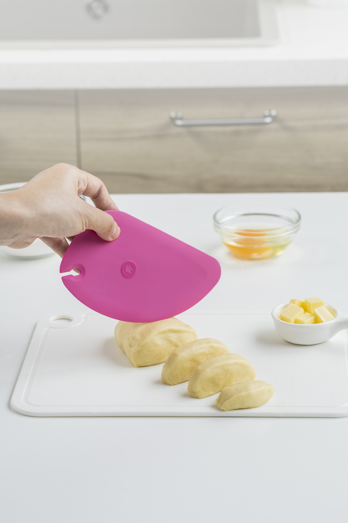 Hand hält einen pinken Silikonschaber über einem Schneidebrett mit geschnittenen Kartoffeln in einer hellen Küche.