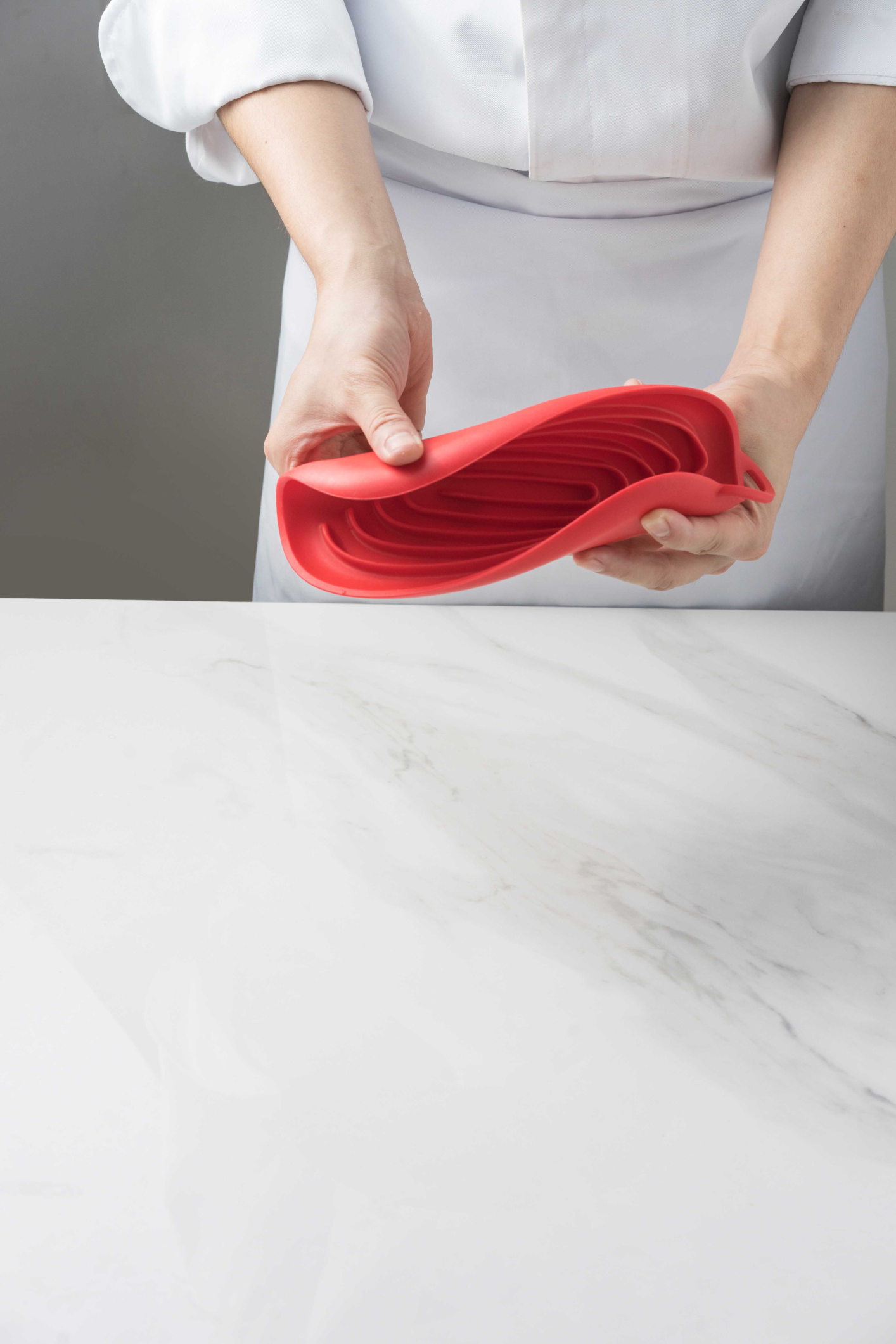 Person in einer Küchenschürze faltet einen flexiblen roten Silikon-Untersetzer auf einer Marmorarbeitsplatte